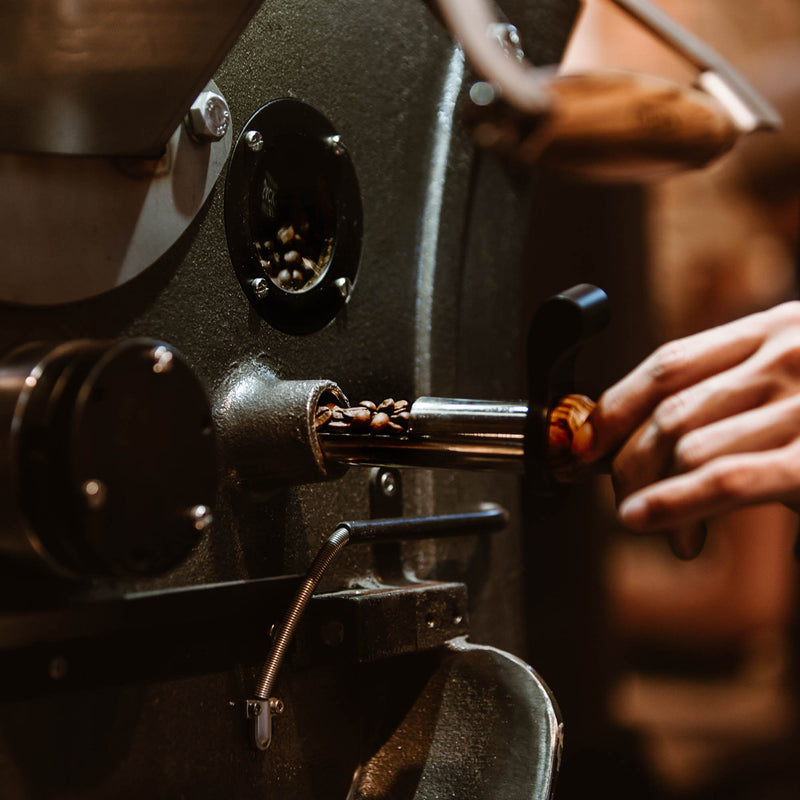 Kaffeebohnen in der Rösttrommel bei Kaffeesack, mit frisch geröstetem Kaffee auf dem Schieber – ein Blick auf die Handwerkskunst des Röstens